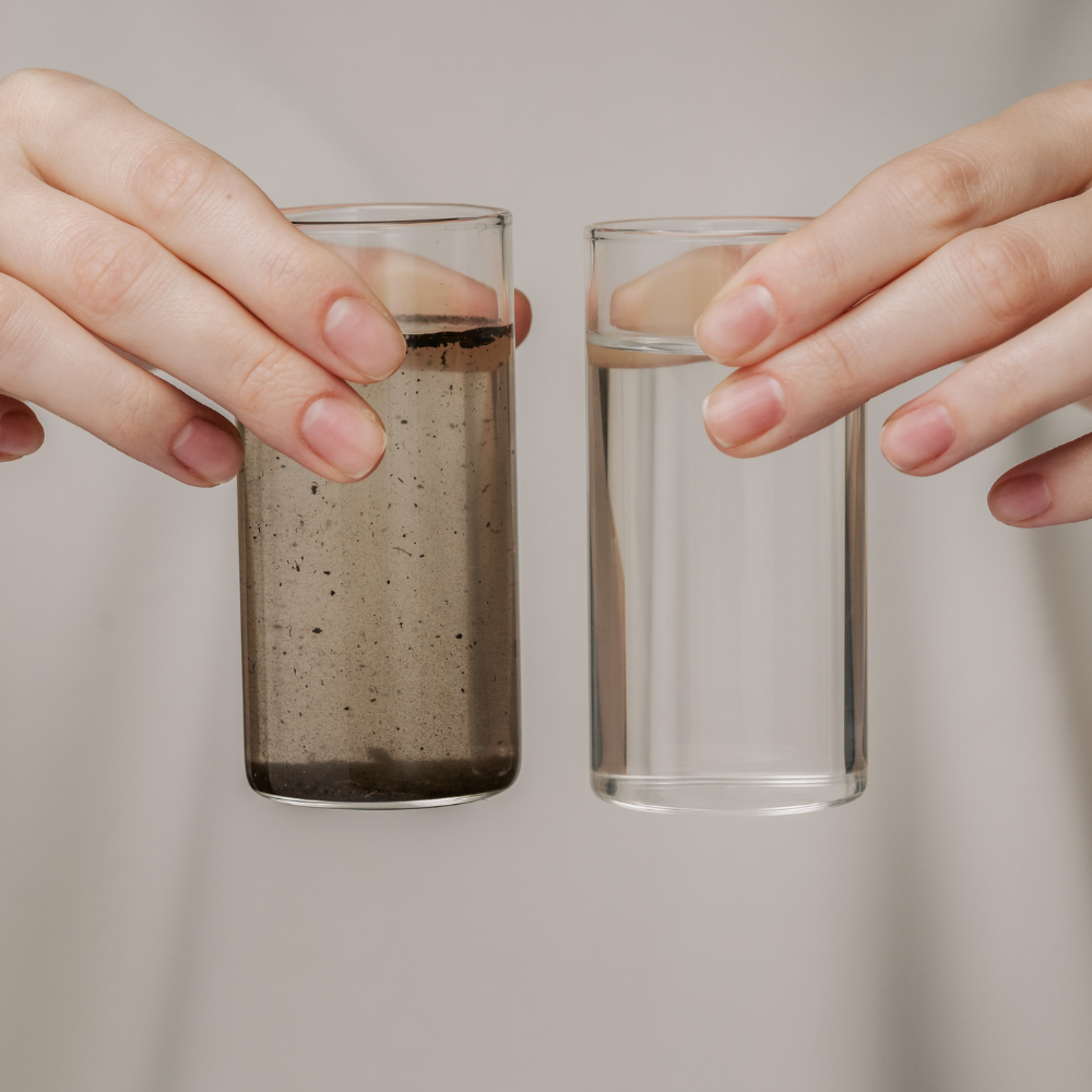 Two hands holding glasses of water and a speckled liquid against a neutral background
